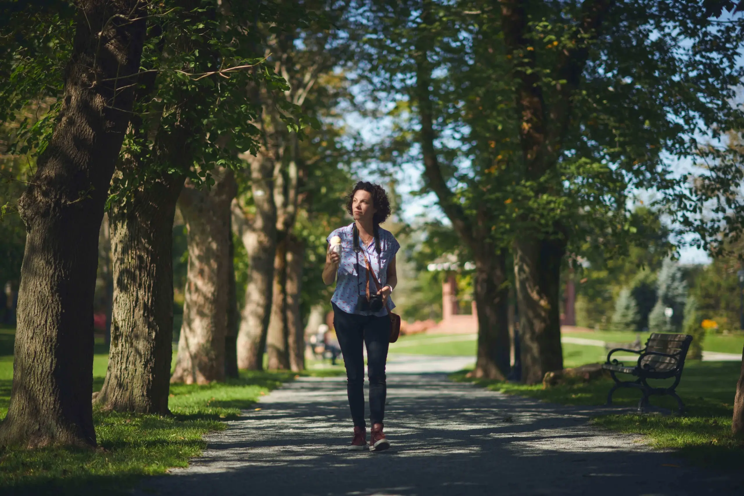 Woman leisurely strolling along a tree-lined path in a serene park.