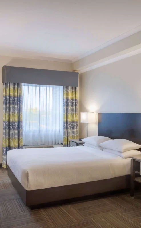 Bright hotel room with a double bed, desk, and natural light from a large window.