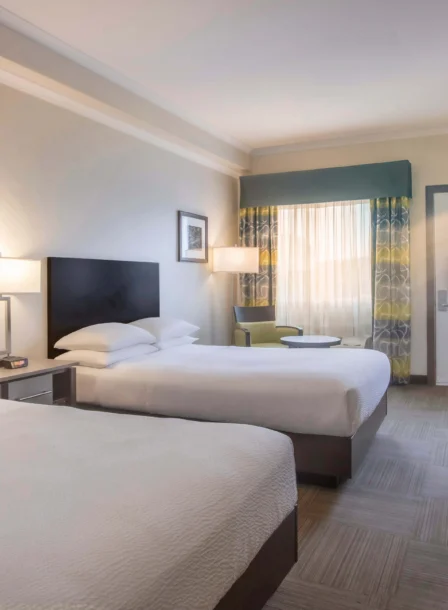 Elegant hotel room with two double beds, cosy lighting, and a workspace near a window.