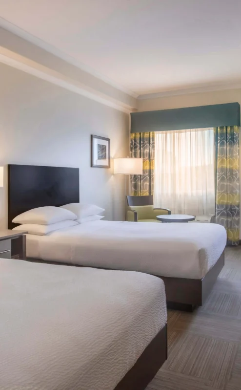 Elegant hotel room with two double beds, cosy lighting, and a workspace near a window.