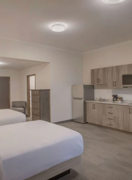 Spacious hotel room with twin beds, kitchenette, and warm lighting.