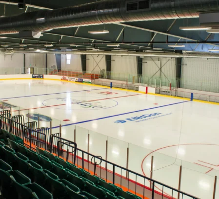 Empty indoor ice rink with family seating and clear boards, calm arena lighting, visible "ElliDohr" rink logo