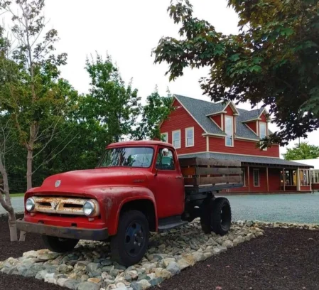 Vintage red flatbed truck on decorative stones outside a family-friendly red inn, trees and gravel drive