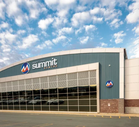 Family arriving at Summit Centre exterior under a bright sky, cars reflected in glass façade