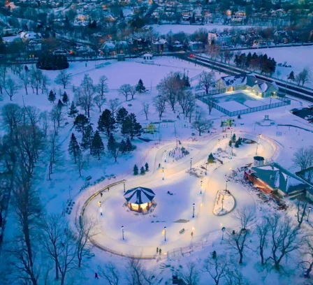 Family enjoying a snowy park with lit pathways at dusk near Crossroads Inn & Suites.