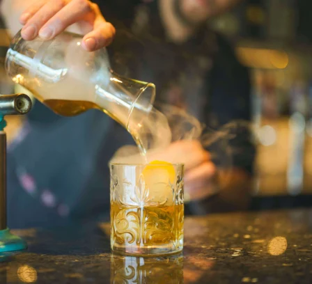 A bartender pours a smoky cocktail at a luxurious bar.
