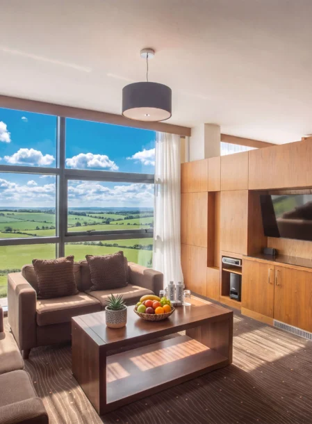 Family relaxing on sofas in a bright suite with countryside view, wooden décor and bed visible
